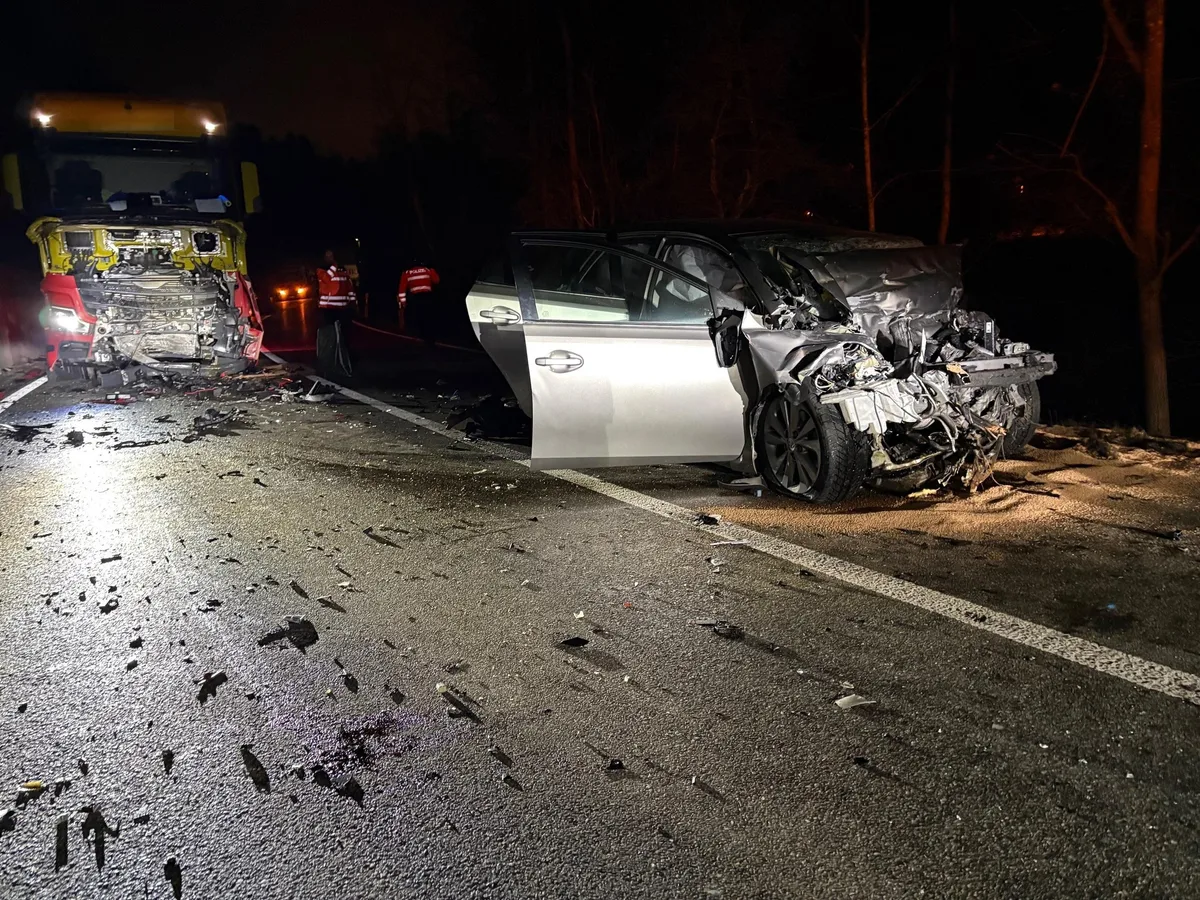 Man sieht das Wrack eines silberfarbenen Autos. Im Hintergrund ein beschädigter Lkw.